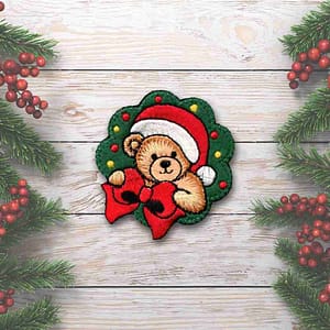 A Christmas Bear Patches (2-Pack) Christmas Embroidered Iron on Patch in a santa hat on a wooden background.