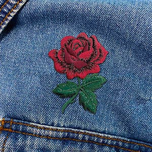 A close up of a Red Rose with Stem Floral Iron On Patch with Sparkling Thread embroidered on a denim jacket.