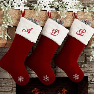 Three red Christmas Stocking Letters - Iron On Monogram Script Letter Patches, Red, Black & White hanging on a fireplace.