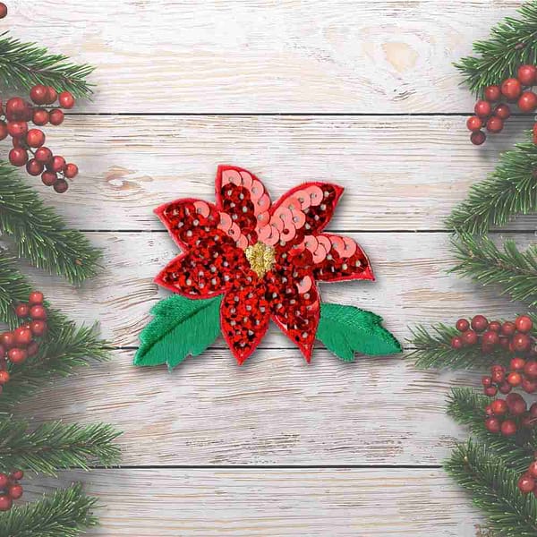 A Poinsettia Patches (2-Pack) Christmas Embroidered Iron On Patch applique on a wooden background.