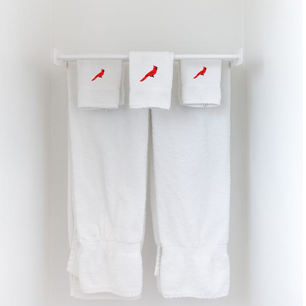 A white towel hangs on a hook with Red Cardinal Patches (5-Pack) Bird Embroidered Iron on Patch Appliques on it.