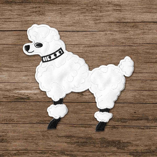 A white 50's Poodle Embroidered Iron On Patch on a wooden surface.