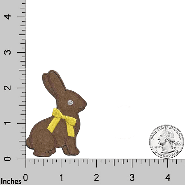 A brown Bunny Patches (2-Pack) Easter Embroidered Iron on Patch Appliques with a yellow bow in front of a ruler.