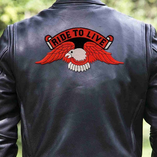 A man wearing a leather jacket with a Ride to Live Orange Eagle Backpatch Iron On Patch on it.