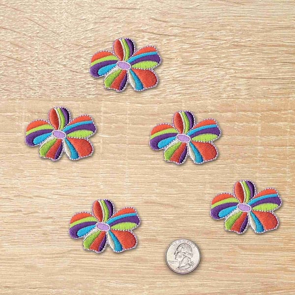 Five Multi-Colored Flower Patches (5-Pack) Flower Embroidered Iron On Patch Appliques on top of a wooden table.