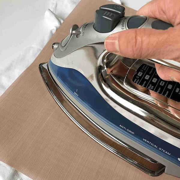A person using a Patch Pressing Sheet to iron a piece of fabric on a table.