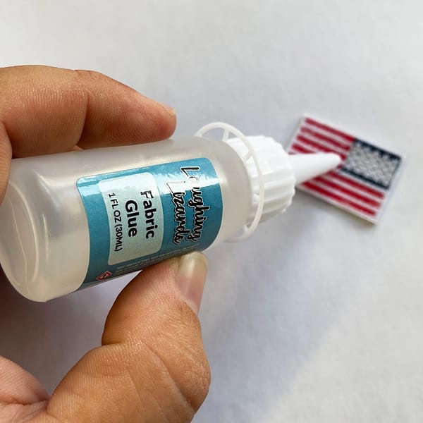 A person holding a bottle of Fabric Glue - 1oz with an american flag on it.