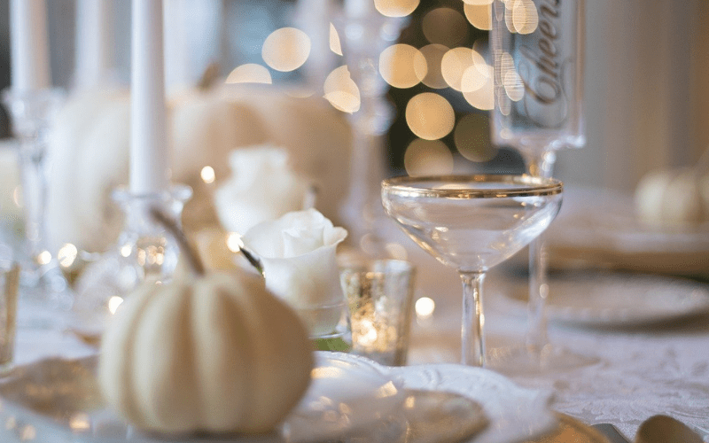 A white and gold table setting with candles and pumpkins.