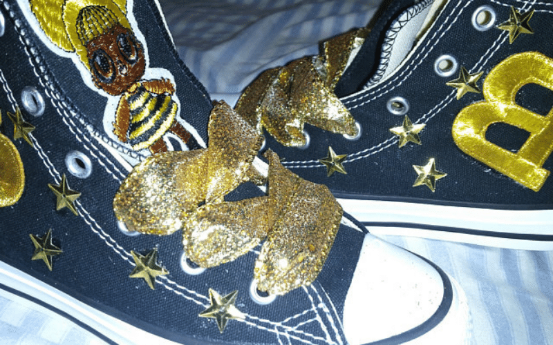 A pair of black and gold converse sneakers with bees on them.